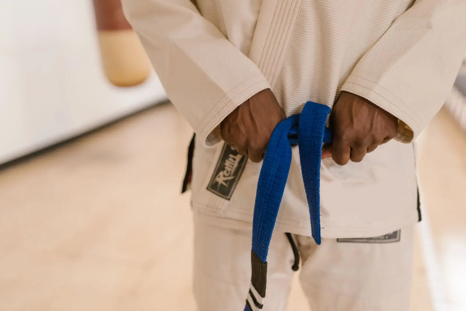 Close-up of a Brazilian Jiu-Jitsu practitioner in a gi holding a belt, illustrating the BJJ ranking system
