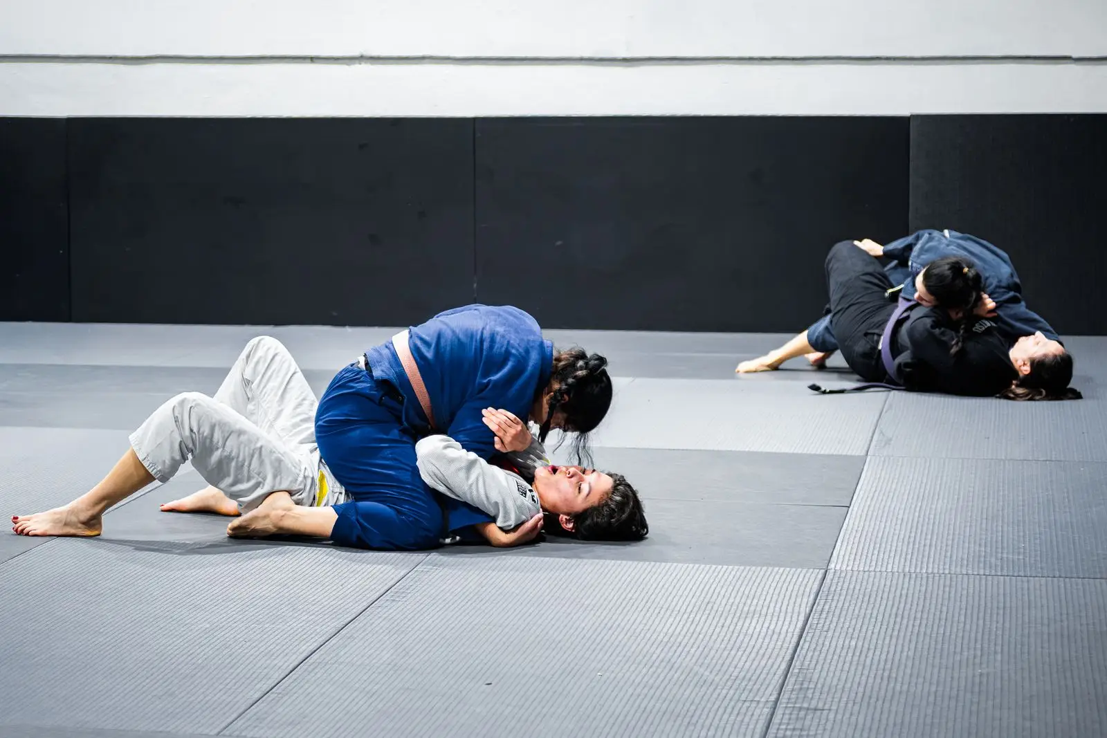 Adults training Brazilian Jiu-Jitsu on the mats at an indoor martial arts gym, similar to Competitive Edge Combat Sports in Florence, SC